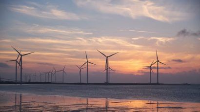 Wind turbines are pictured, along with water and a sunrise or sunset.