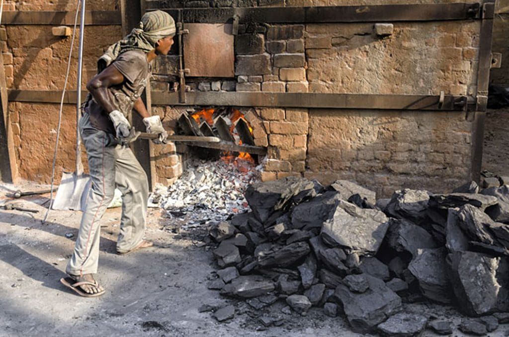 man shoving coal into oven in India