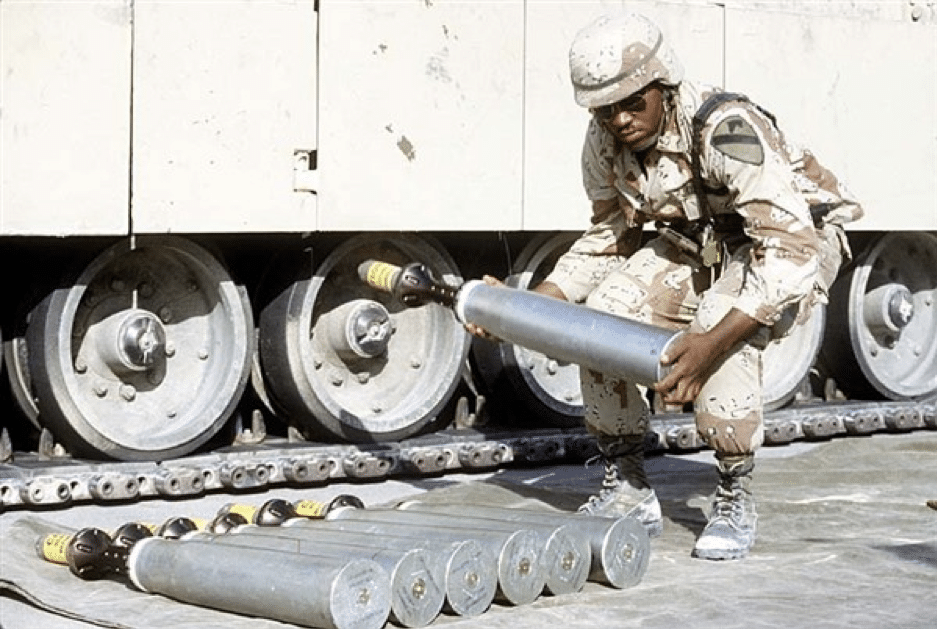 An ammunition specialist carries a 105 millimeter armor-piercing round to be used in an M-1 Abrams main battle tank during Operation Desert Shield in 1991. The object on the nose of the round is a sabot, a cover that protects and stabilizes the round's needle-like depleted uranium penetrator, then falls away as the projectile leaves the gun barrel. (Photo courtesy of the US Defense Department)