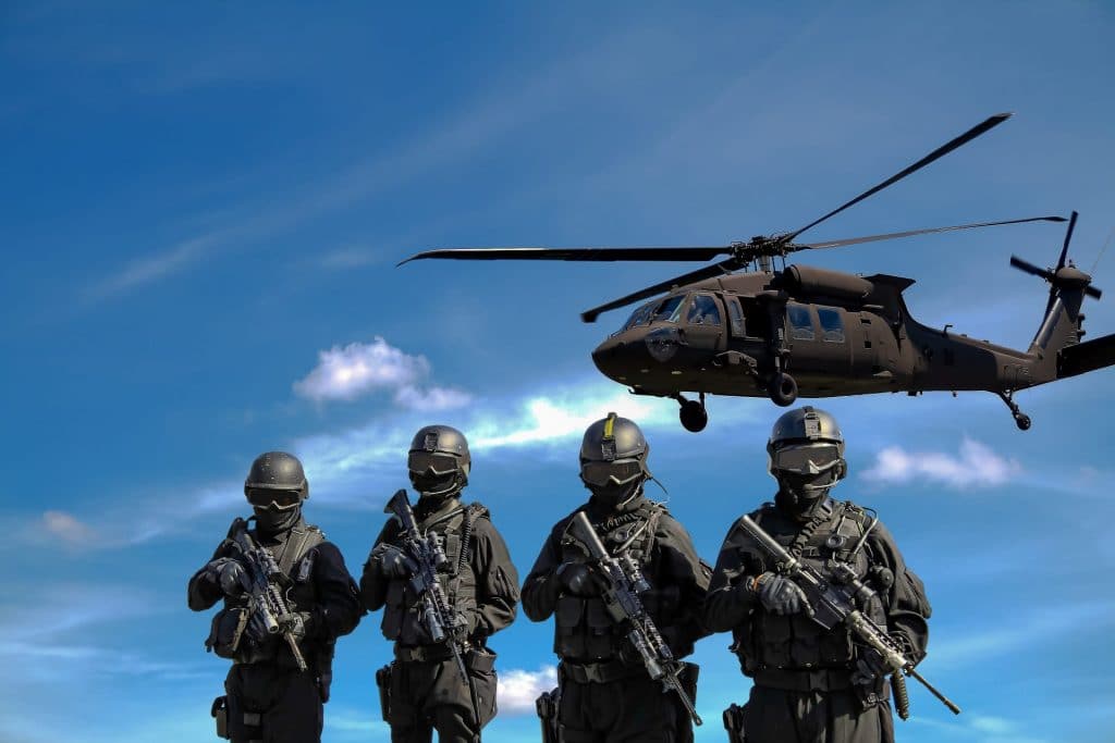 Four soldiers carrying rifles near helicopter under blue sky. Credit: Somchai Kongkamsri. Access via Pexels. Free to use.