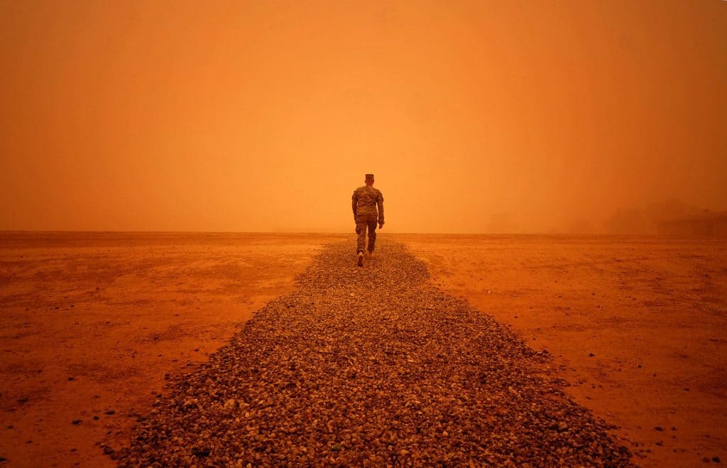 A man in military camo walks through a sandstorm in Iraq