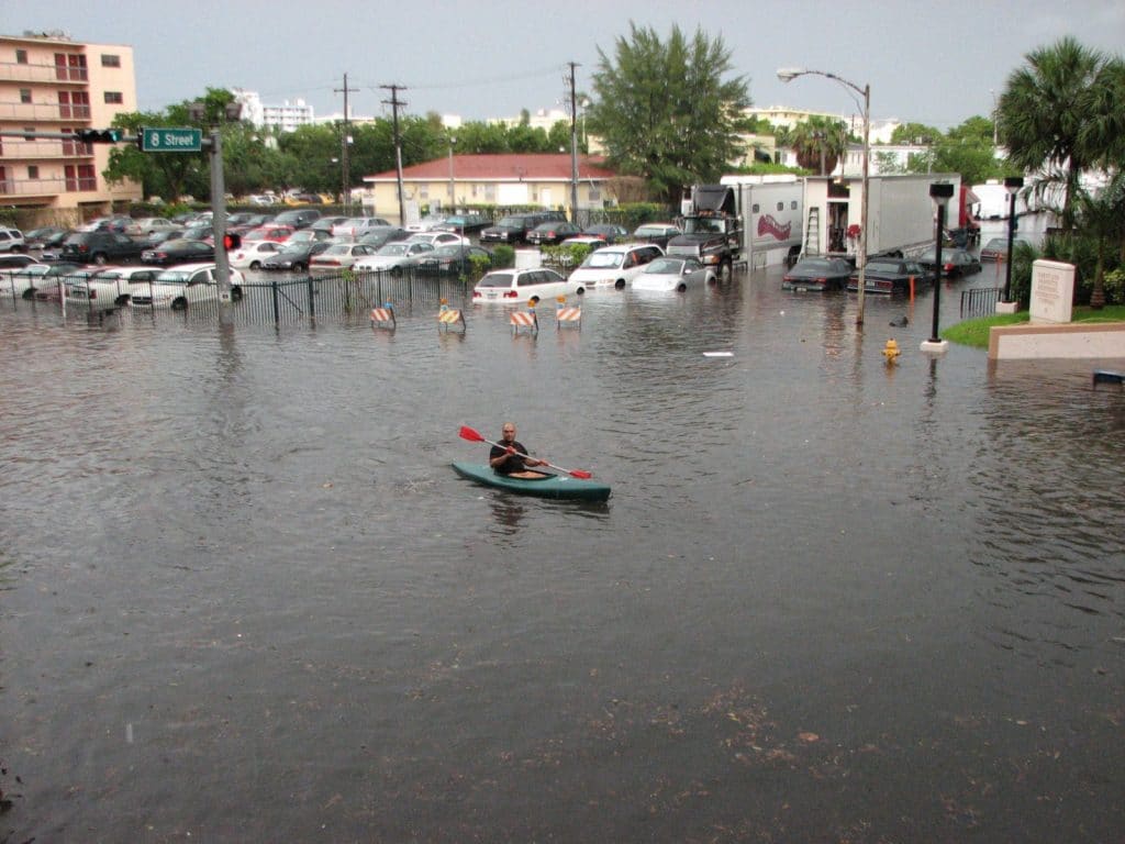 A man kayaks down a flooded street in front of flooded cars