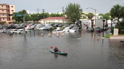 A man kayaks down a flooded street in front of flooded cars