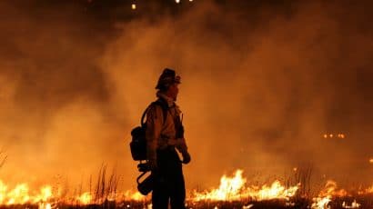 lone firefighter standing in front of flames