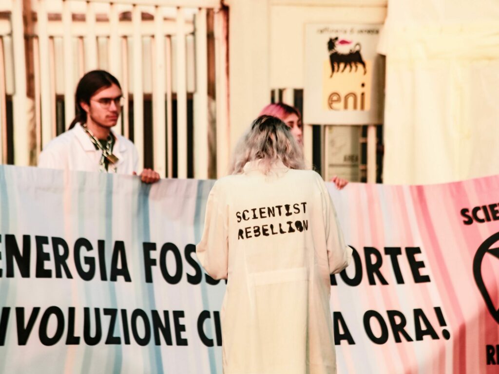 Woman in white coat reading Scientist Rebellion stands in front of a sign in Italian held by other activists.