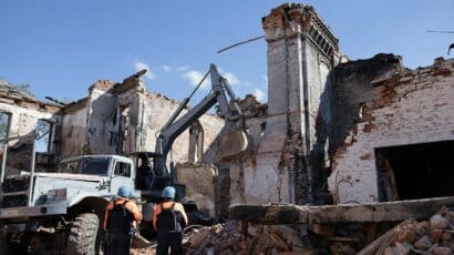 destroyed buildings in ukraine, two workers and a truck in foreground
