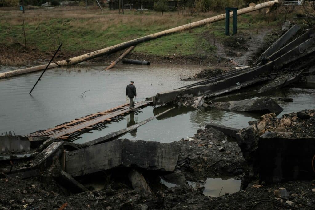 a man crosses a destroyed bridge holding water bottles