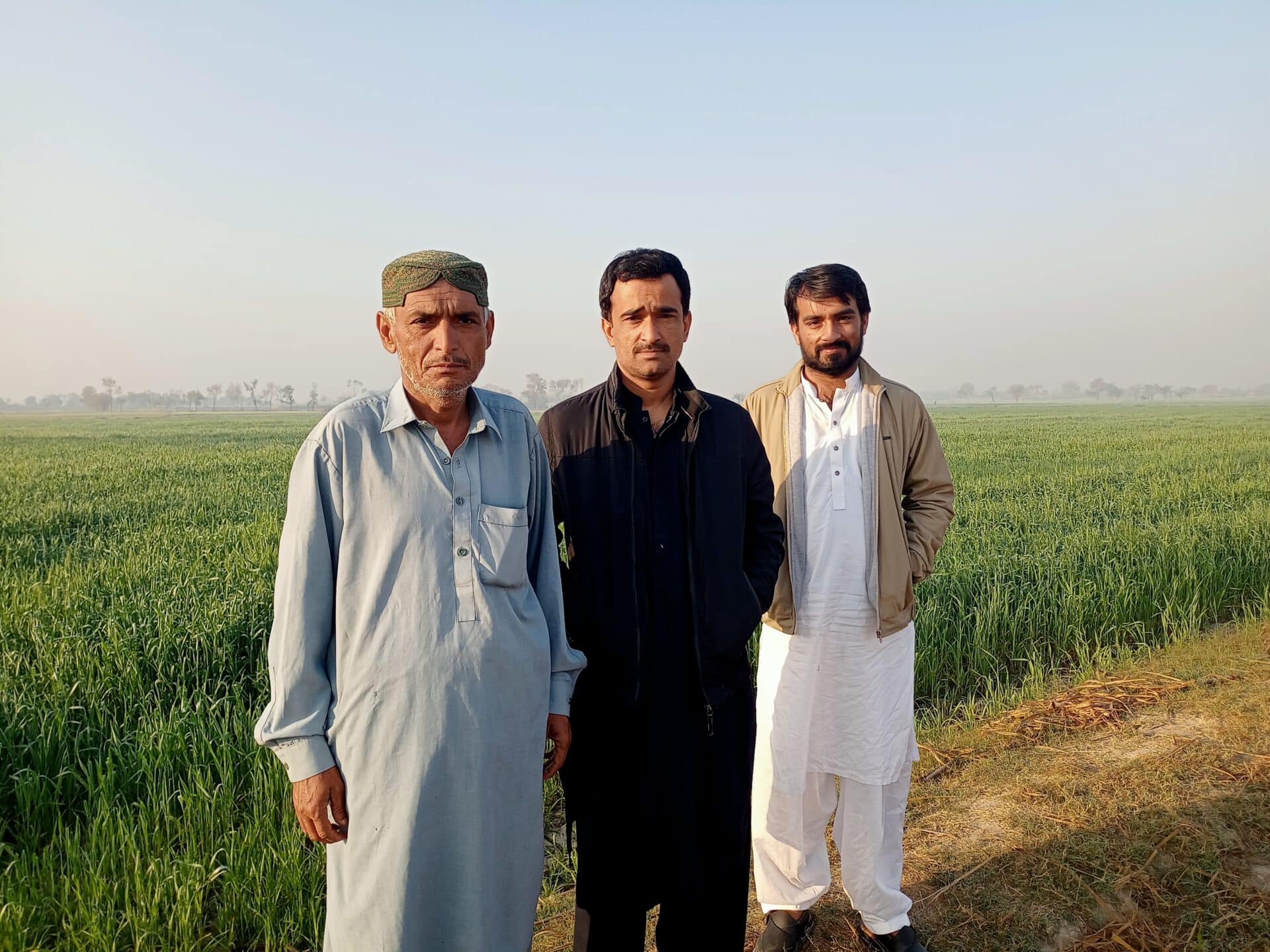 three men stand in front of a field