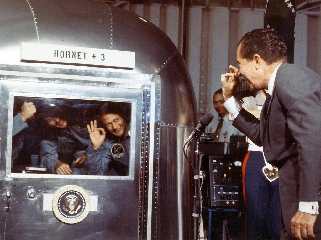 Quarantined in a modified Airstream trailer after returning from the Moon on July 24, 1969, the Apollo 11 astronauts exchange "a-OK" signs with President Nixon.
