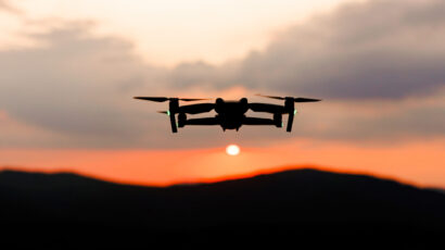 The silhouette of a drone flying over the mountains line at sunset