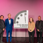Speakers standing in front of the Doomsday Clock