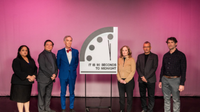 Speakers standing in front of the Doomsday Clock