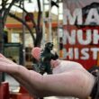 toy Godzilla held in a hand in front of Make Nukes History sign