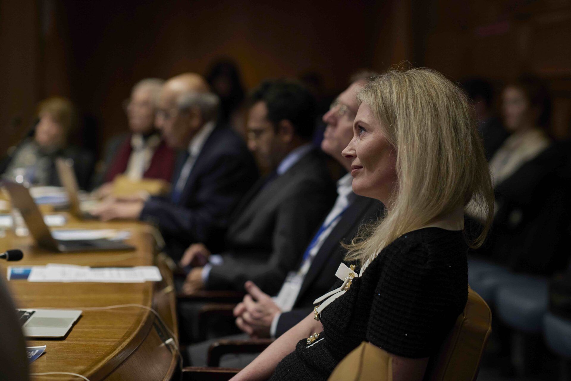 A woman sits at a wooden table alongside other biosecurity and virology experts.