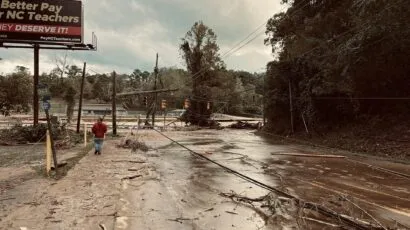 A man walks towards a flooded river, across a mud-strewn road.