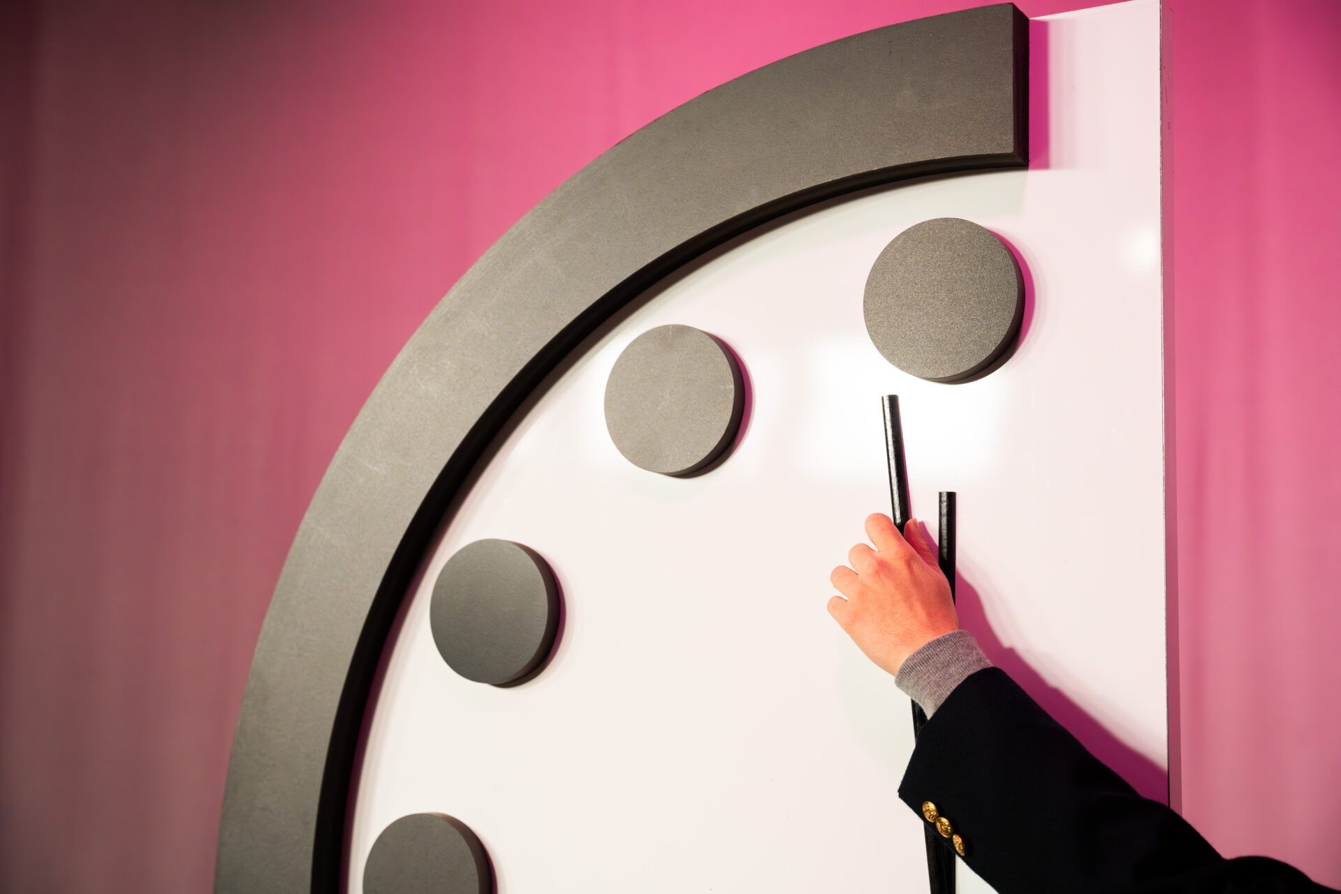 A hand holds the minute hand of the Doomsday Clock.