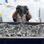 A person holds a large handful of e-waste up in front of their face above a large container of e-waste.