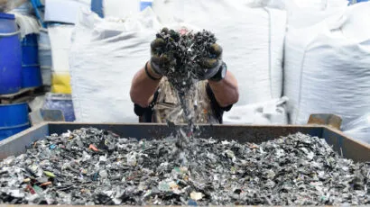 A person holds a large handful of e-waste up in front of their face above a large container of e-waste.