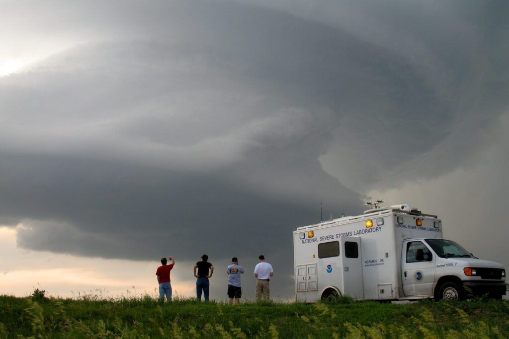 four people and a truck in the foreground, a thundercloud in the distance