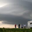 four people and a truck in the foreground, a thundercloud in the distance