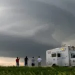 four people and a truck in the foreground, a thundercloud in the distance