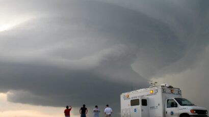 four people and a truck in the foreground, a thundercloud in the distance