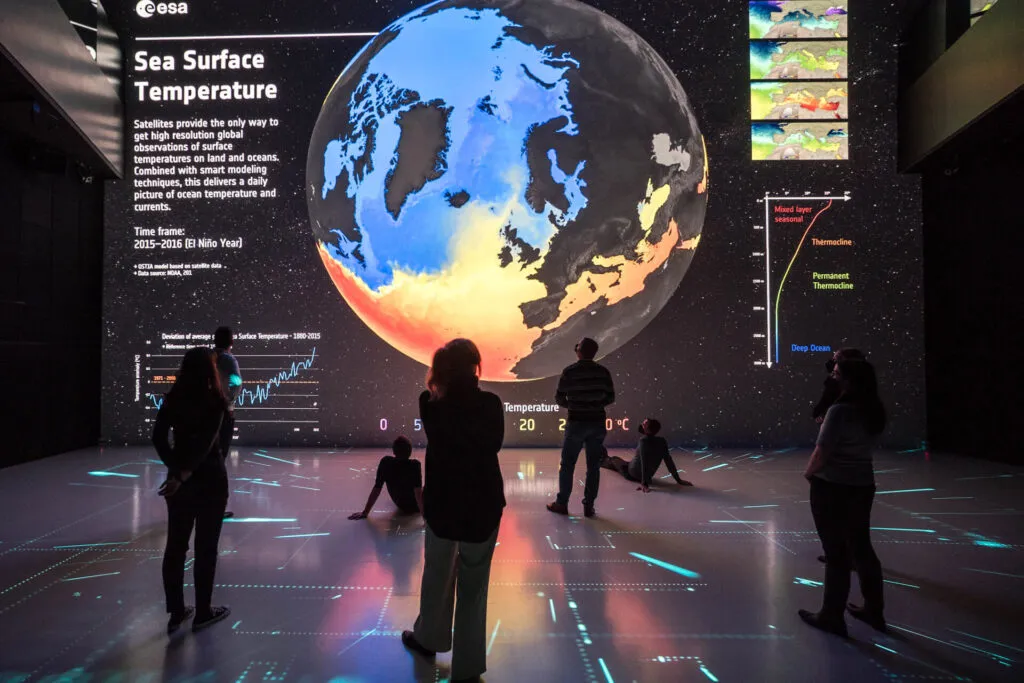 People looking at a large projection of the Earth showing a map of sea surface temperatures