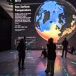 People looking at a large projection of the Earth showing a map of sea surface temperatures