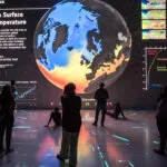 People looking at a large projection of the Earth showing a map of sea surface temperatures