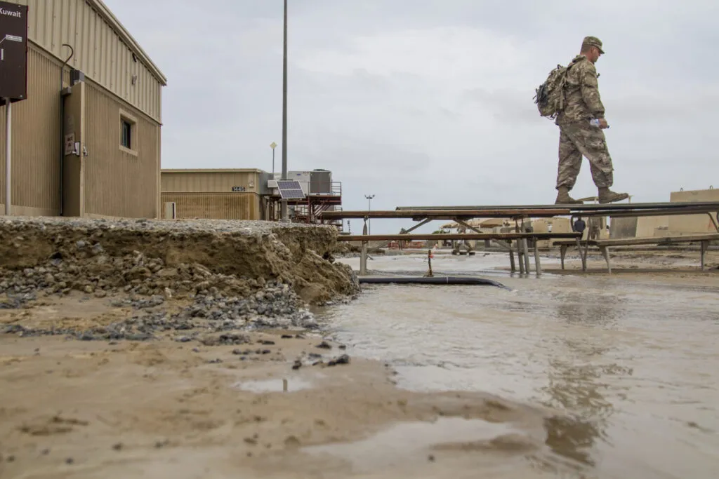 soldier walking on makeshift bridge over muddy flooded area