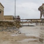 soldier walking on makeshift bridge over muddy flooded area