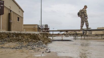 soldier walking on makeshift bridge over muddy flooded area