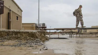 soldier walking on makeshift bridge over muddy flooded area