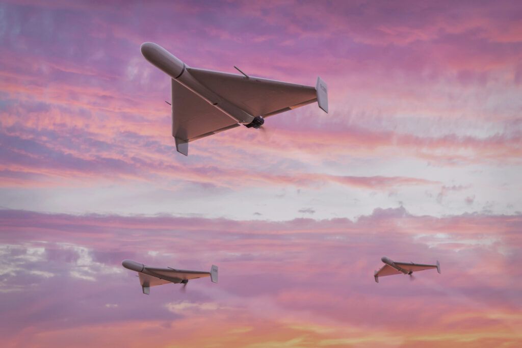 Three drones flying in a pink and orange sky