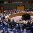 People sit in a large, circular conference room, attending a meeting at the United Nations Security Council.