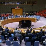 People sit in a large, circular conference room, attending a meeting at the United Nations Security Council.