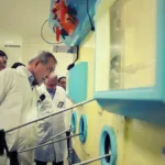 A group of men in white lab coats observe equipment inside a laboratory.