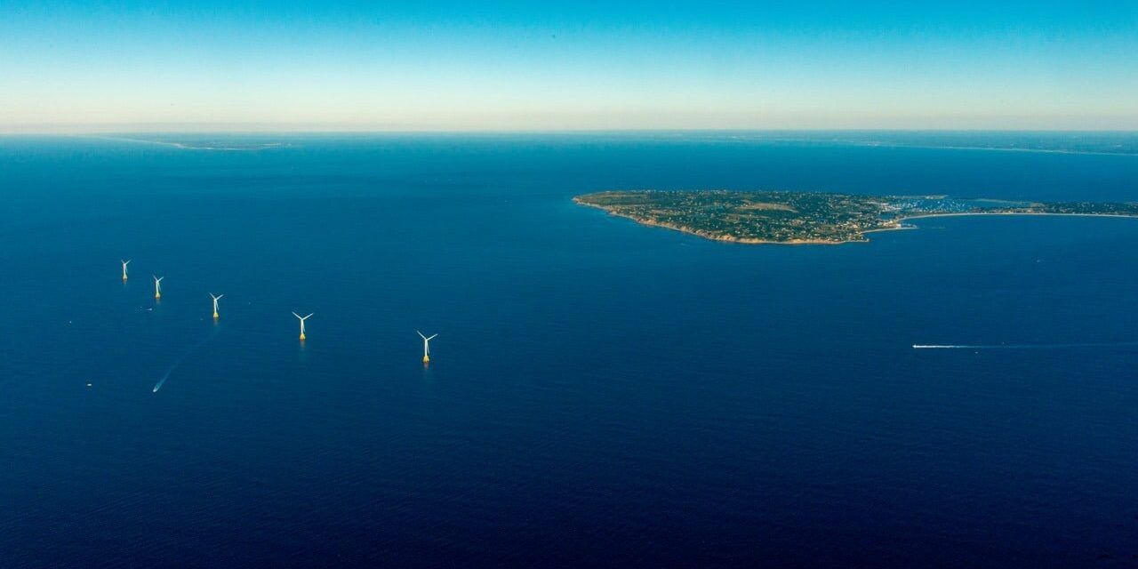 Looking west at Block Island from the air with its five offshore windmills, north is to the right in this aerial photo. The tip of Long Island can just be made out on the far left horizon; immediately behind Block Island on the right one can make out the line of white surf that marks the Connecticut shoreline. Image courtesy of Deepwater Wind. 