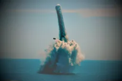 A submarine-launched missile emerges vertically from the ocean, creating a large splash and plume of water and vapor.